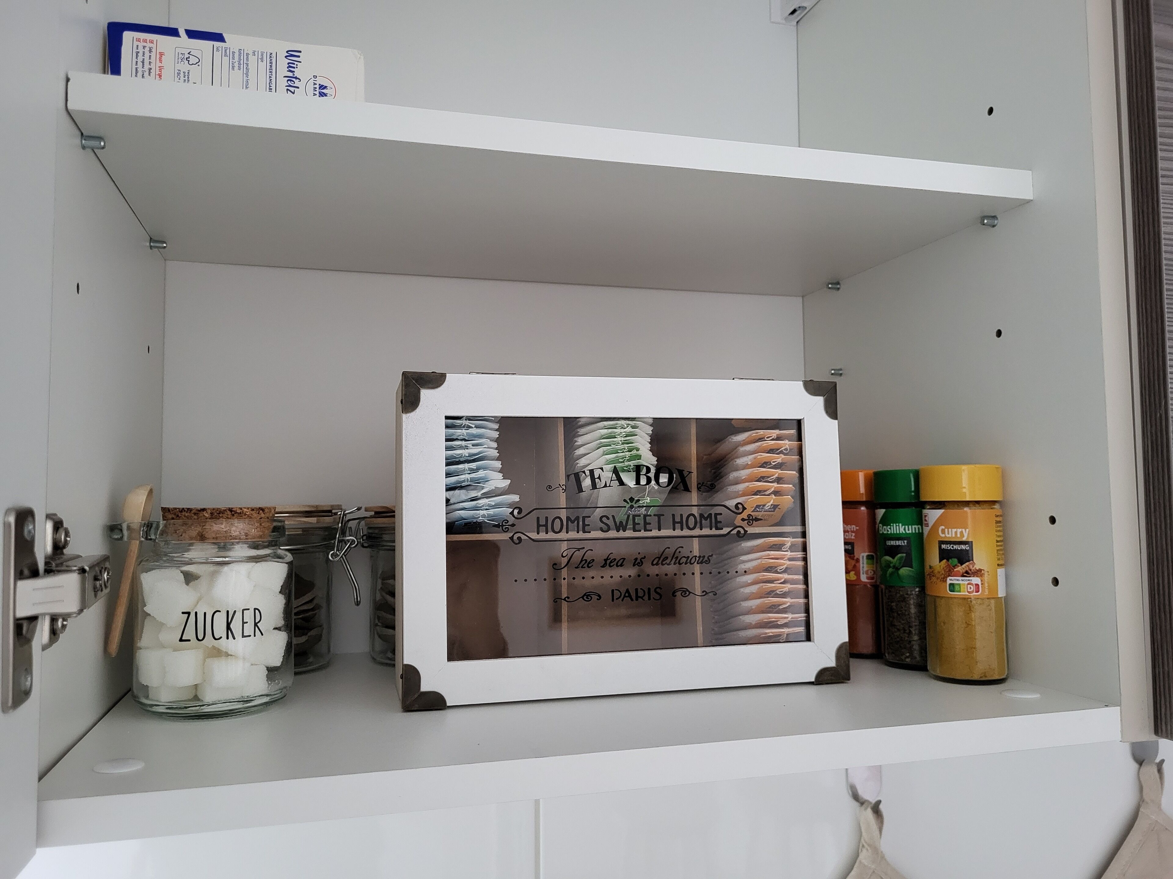Ein Küchenschrank mit einer Teedose mit dem Aufdruck "Home Sweet Home" und verschiedenen Gewürzen.