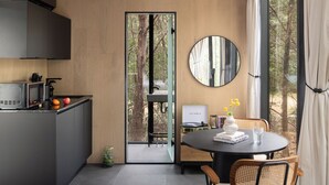 Een moderne keuken met een eethoek, een ronde spiegel en uitzicht op het bos door een glazen deur.