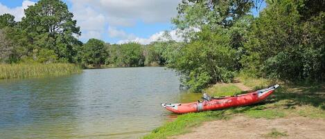 A red canoe on a calm riverbank with dense greenery and trees in the background.