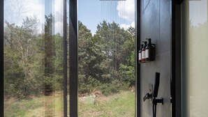 A modern bathroom with a large window, a shower, and a sink. - The Bloom ÖÖD Mirror House (Austin) (Bastrop)