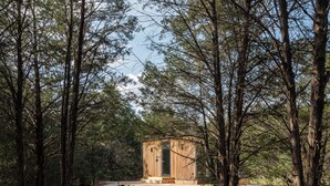 Una baita di legno con una terrazza, circondata da alberi alti in una foresta.
