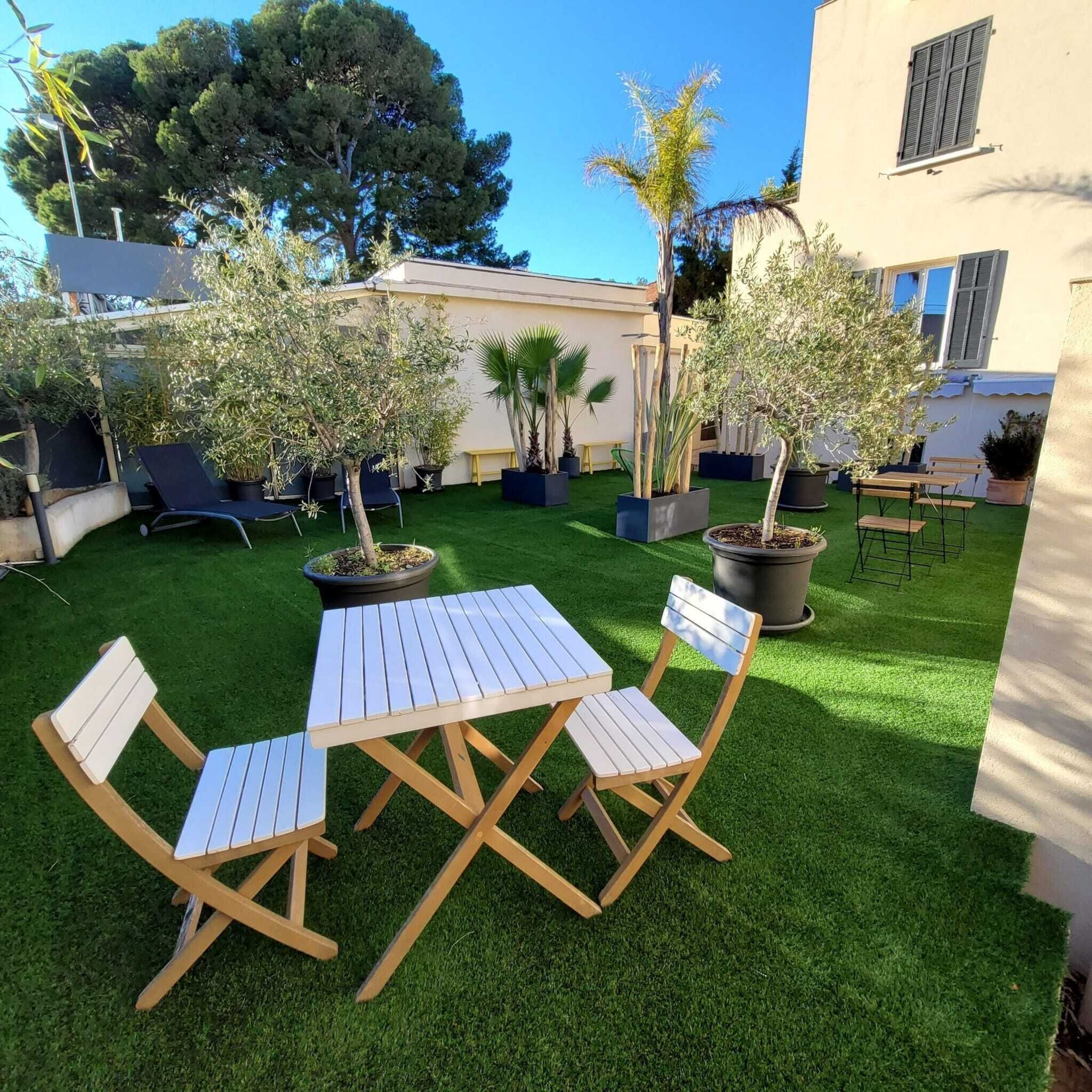 Een terras met een tafel en stoelen, omringd door potplanten en een gebouw op de achtergrond.