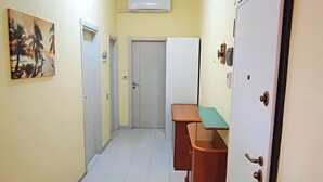 A hallway with a tiled floor, a painting on the left wall, a whiteboard, and a door on the right.
