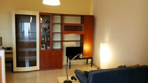 A living room with a TV, a cabinet with bottles, a sofa, and a lamp.