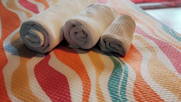 A bed with a colorful striped blanket and three rolled-up towels.