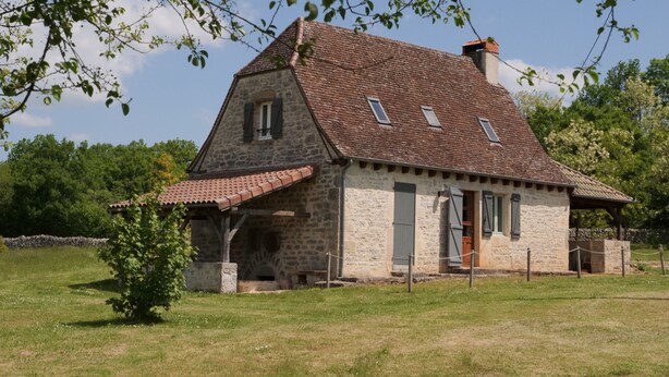 A stone house with a sloped roof, a small porch, and a fenced yard. - MAS DE MAGAL GRAMAT (Gramat)