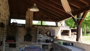 An outdoor kitchen area with a table and chairs, a hanging light fixture, and a stone oven. - MAS DE MAGAL GRAMAT (Gramat)