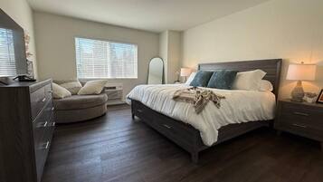 A bedroom with a bed, a dresser, a chair, and a window with blinds.