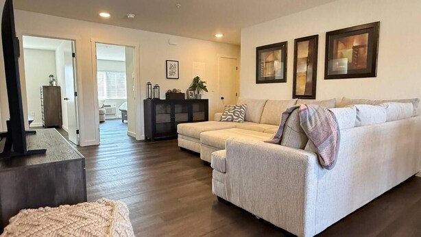 A living room with a sofa, a coffee table, and a TV. There are framed pictures on the wall and a plant on a side table. - Homestead Village - Two Bedroom Condo Balcony (Sandpoint)