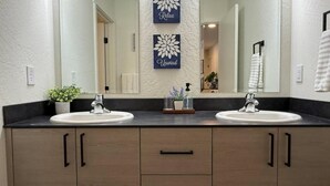 A bathroom with two sinks, a mirror, and decorative wall art. - Homestead Village - Two Bedroom Condo Balcony (Sandpoint)