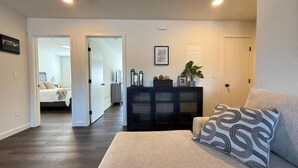 A living room with a sofa, a cabinet, and a door leading to a bedroom. - Homestead Village - Two Bedroom Condo Balcony (Sandpoint)