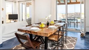 A dining area with a wooden table set for four, a television in the corner, and a view of the sea through large sliding doors. - Villa Roxana, by the sea and with private pool (ES CASTELL)