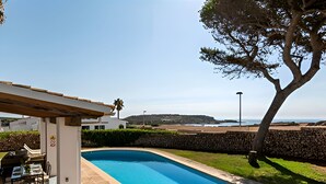 A swimming pool with lounge chairs and a pergola, surrounded by a stone wall and a view of the sea. - Villa Roxana, by the sea and with private pool (ES CASTELL)