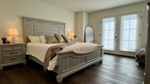 Une chambre à coucher avec un grand lit, une table de chevet avec une lampe, une commode et une porte avec une fenêtre.