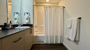 Une salle de bain équipée d’un lavabo, d’un miroir, d’un porte-serviettes, d’un rideau de douche et d’une serviette accrochée au mur.