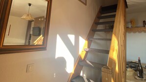 A staircase with wooden steps and a handrail, leading to a room with a mirror, framed pictures, and a ceiling with exposed beams. - Duplex 6 pers at the foot of the slopes Comfort, charm & mountain view Ski in & out (Risoul)