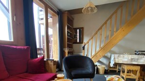 A cozy living room with a sofa, a table with snacks and drinks, a chair, and a staircase. - Duplex 6 pers at the foot of the slopes Comfort, charm & mountain view Ski in & out (Risoul)