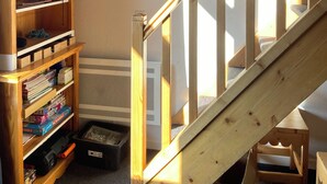 A staircase with wooden railings, a wooden bookshelf filled with various items, a framed picture on the wall, and a hanging light fixture. - Duplex 6 pers at the foot of the slopes Comfort, charm & mountain view Ski in & out (Risoul)