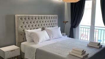 A modern bedroom with a tufted headboard, a bedside table with a drawer, a large bed with a quilted duvet, and a hanging light fixture.