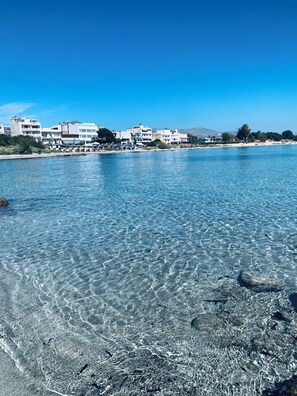 En kuststad med klart vatten, byggnader längs strandlinjen och en stenstrand.
