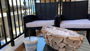 A balcony with wicker furniture, a glass table, and a drink container. - F.K.Apartments is situated 50m away from the beach and 10km from the ATH.Airport (Artemis)