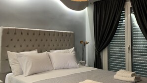 A modern bedroom with a tufted headboard, a large bed with a quilted bedspread, two pillows, a bedside table with a vase, and a hanging light fixture. - F.K.Apartments is situated 50m away from the beach and 10km from the ATH.Airport (Artemis)