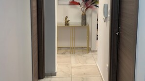 A hallway with marble flooring, a console table with decorative items, and a modern light fixture. - F.K.Apartments is situated 50m away from the beach and 10km from the ATH.Airport (Artemis)