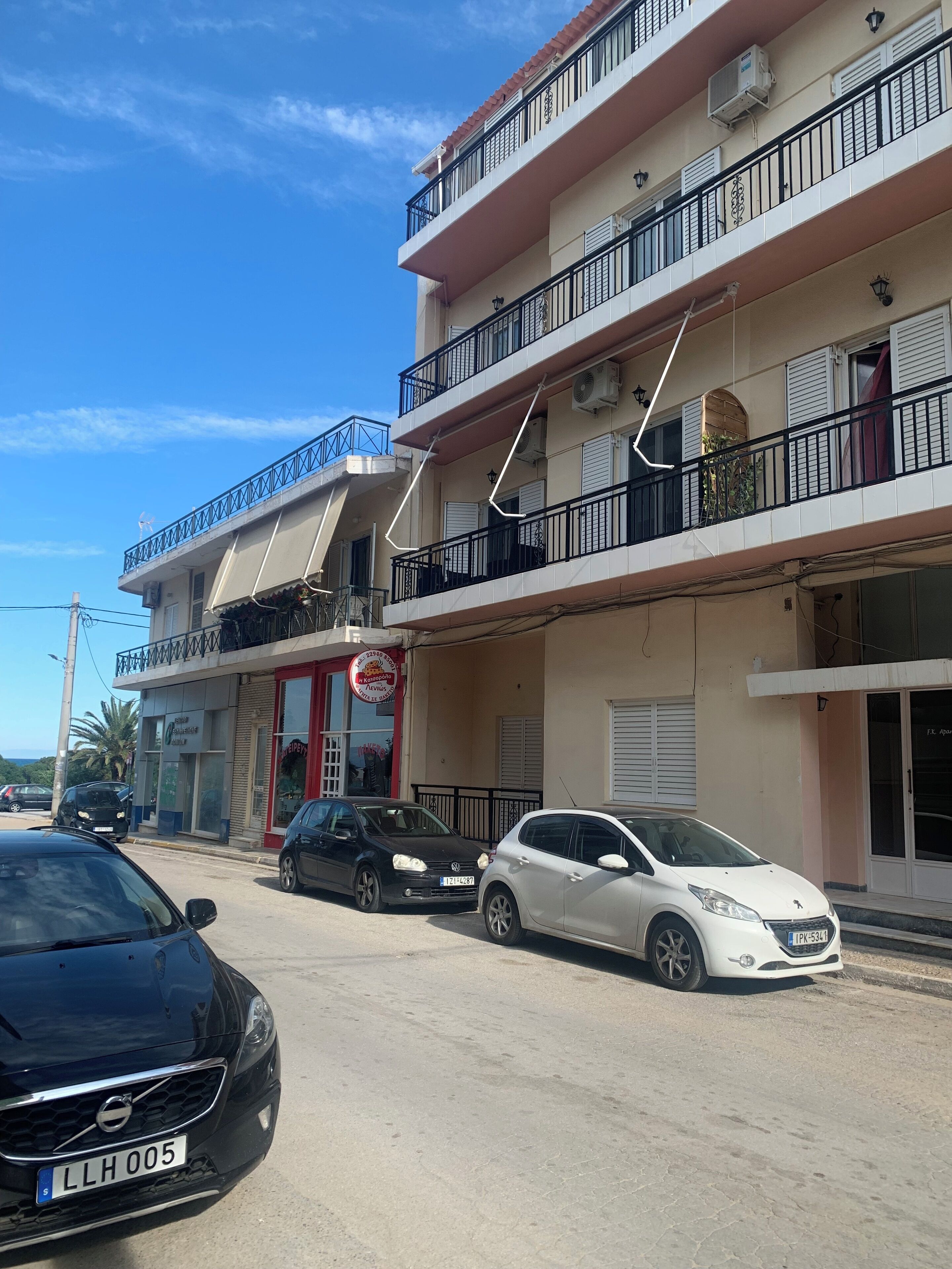 A multi-story building with balconies, a red storefront, and parked cars.