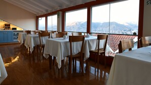 A restaurant with tables set for dining, large windows with a mountain view, and a kitchen area in the background. - Tandapata Boutique Hotel (Cusco)