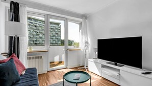 A modern living room with a sofa, a glass coffee table, a flat-screen TV, and a balcony with a city view.
