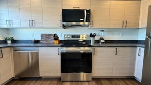 A modern kitchen with light wood cabinets, stainless steel appliances including a microwave, oven, and dishwasher, and a granite countertop.