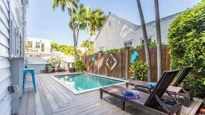 A wooden deck with a swimming pool, lounge chairs, and a wooden fence with a decorative design. - Margaretaville (Key West)