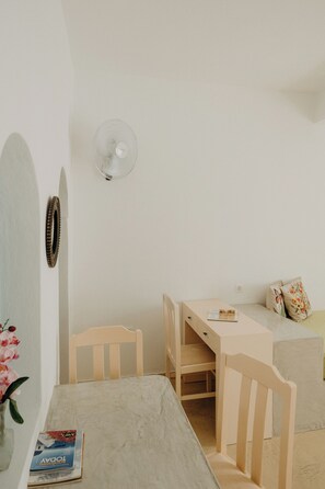 A minimalist room with a wooden desk, a chair, a small table, and a wall-mounted fan.