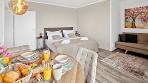 Una camera d'albergo moderna con un tavolo per la colazione ordinato, un divano confortevole e un ampio letto con testiera.