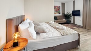 Una moderna camera d'albergo con un letto grande, un comodino con una lampada, una TV a schermo piatto montata a parete e una pianta in vaso.