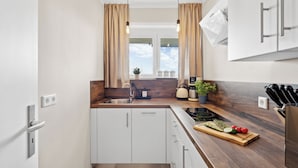 Una cucina moderna con mobili bianchi, un piano di lavoro in legno, un lavello e una finestra con tende.