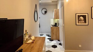 A compact living space with a wooden dining table, a TV, and a kitchenette in the background. - The Vinci Residence • Premium Studio | Kraków Old Town (Kraków)