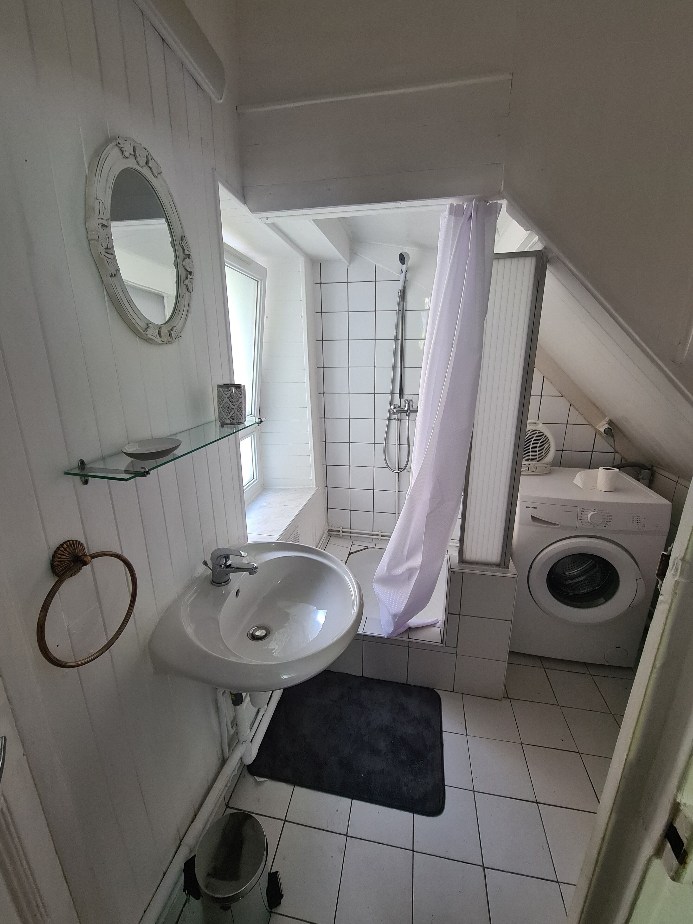 Een badkamer met een wastafel, spiegel, douche en wasmachine.