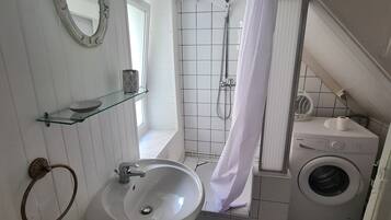 Een badkamer met een wastafel, spiegel, douche en wasmachine.