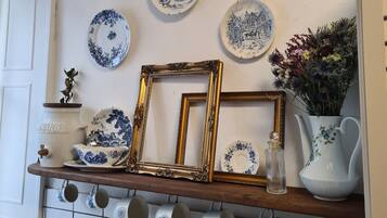 Un mur orné de différents modèles d’assiettes décoratives et une étagère en bois sur laquelle sont posés des photos encadrées, un pichet et un vase rempli de fleurs.