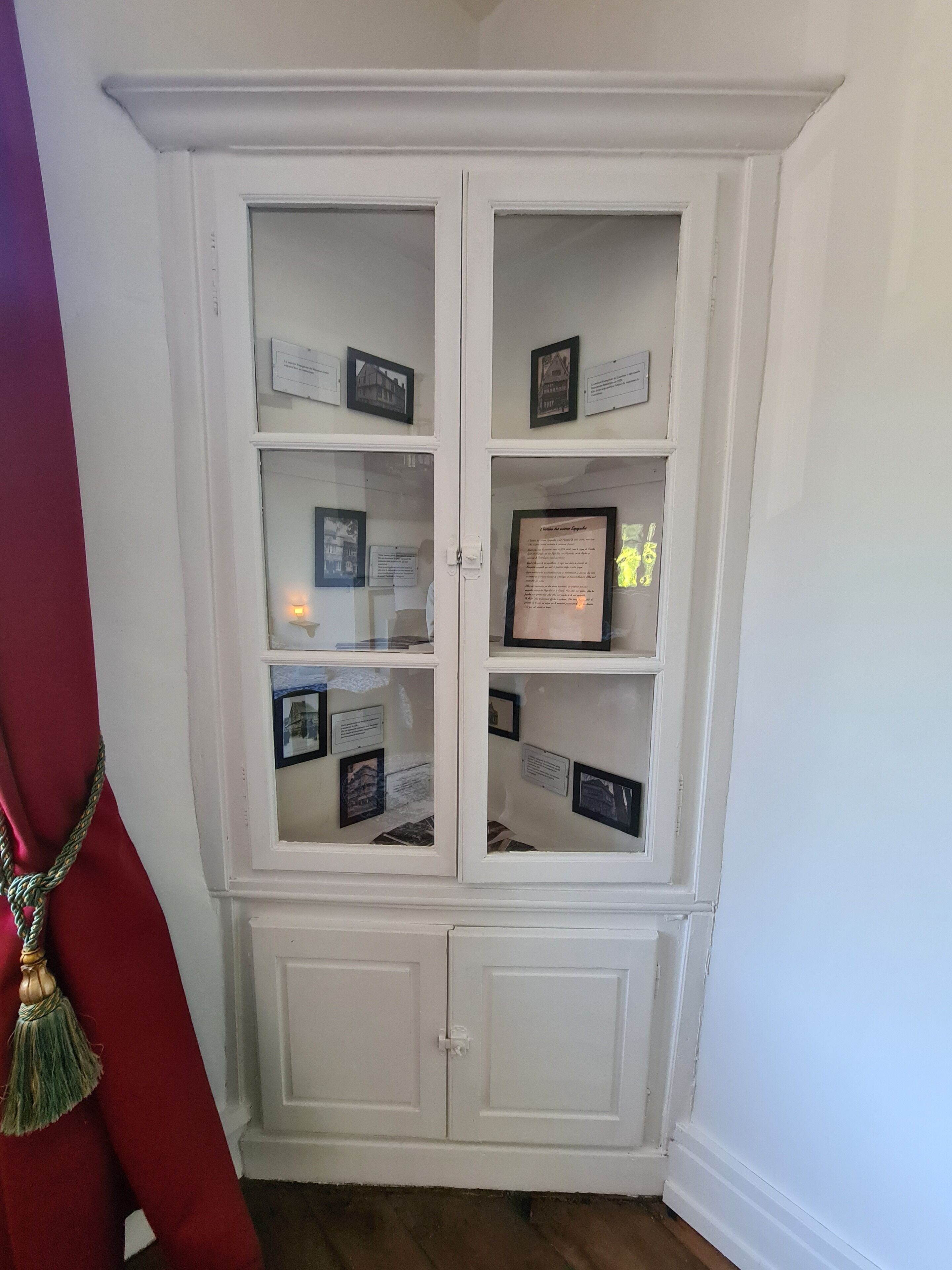 Een witte vitrinekast met glazen deuren, gevuld met ingelijste foto's en informatieborden.