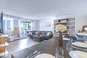 En moderne stue med en grå sofa, et sofabord og et spiseområde med tallerkener og bestik.