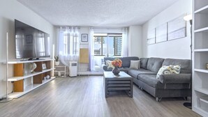 A modern living room with a grey sofa, a flat-screen TV, and a coffee table. - Cozy & Spacious 2BR at Stampede w/ Parking, AC (Calgary)