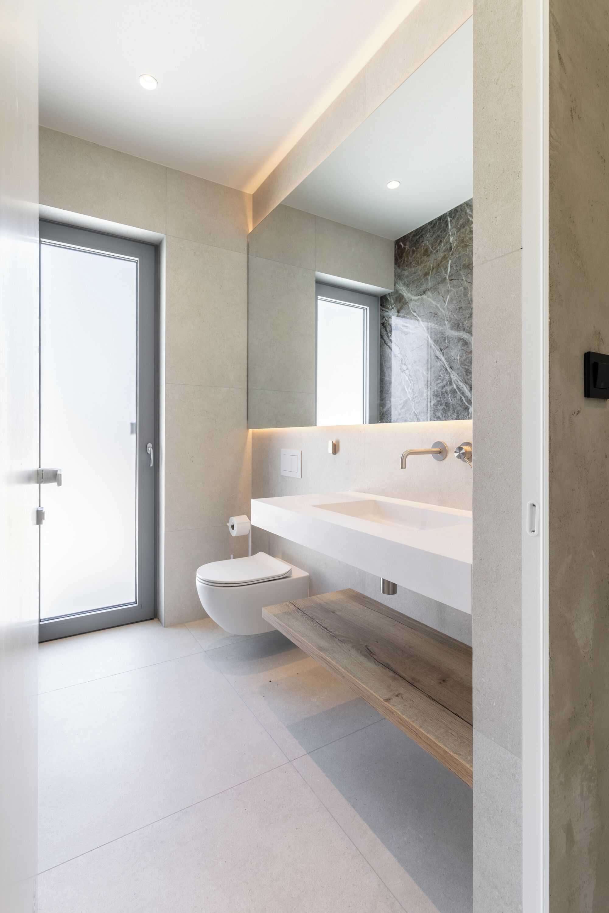 A modern bathroom with a large mirror, two sinks, and a toilet.