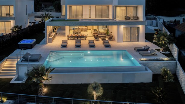 Ein modernes, zweistöckiges Haus mit Schwimmbad, Sitzgelegenheiten im Freien und einer gut beleuchteten Terrassenfläche.