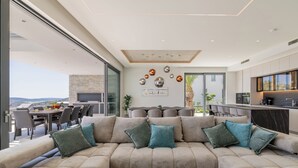 Ein modernes Wohnzimmer mit einem beigefarbenen Ecksofa, einem Essbereich und einer Küche.