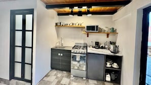 A compact kitchen with a gas stove, microwave, and a small refrigerator. There are wooden shelves above the stove and a tiled floor. - EL MIRADOR, Casa EA Oaxaca, Historic Center, Terrace and Mountain View. (OAXACA DE JUAREZ)