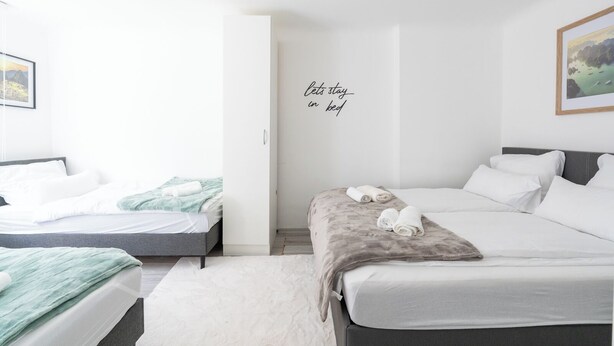 Une chambre d’hôtel avec deux lits, un mur blanc orné d’une inscription « bonjour, restez au lit », et un tableau encadré accroché au mur.