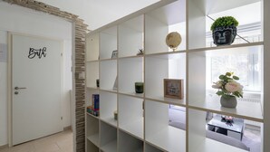 Un couloir avec une porte blanche portant l’inscription « Salle de bain » et une étagère blanche contenant divers objets.