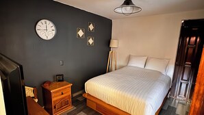 Quarto com cama, mesa de cabeceira, penteadeira, relógio de parede e luminária no teto.